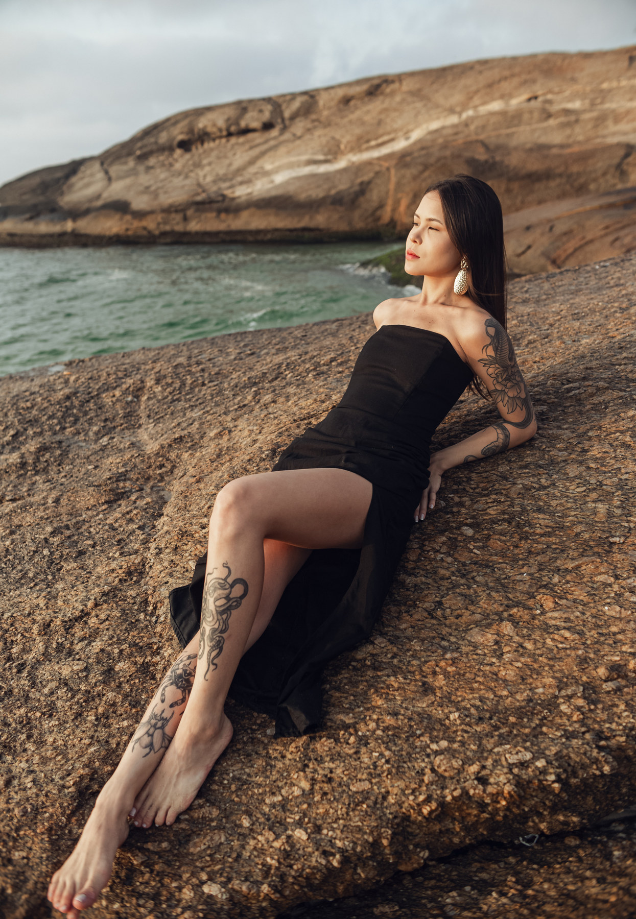 Model im schwarzen Kleid auf Küstenfelsen